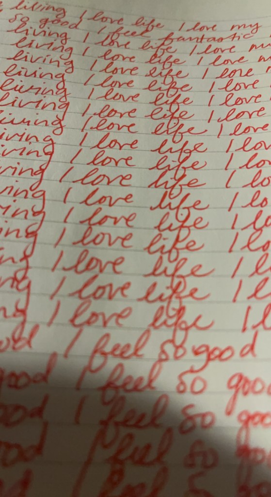A close-up of handwritten notes featuring repeated phrases 'I love life' and 'I feel so good' in red ink on lined paper.