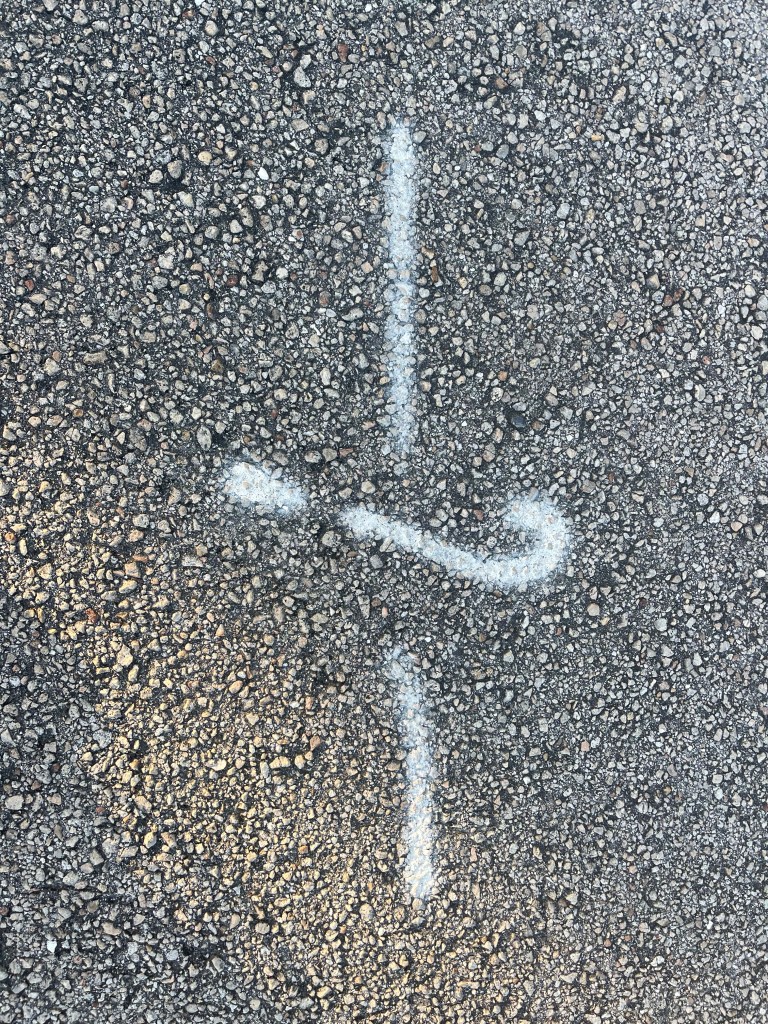 A white, chalk-like symbol drawn on a textured asphalt surface, resembling an abstract design.
