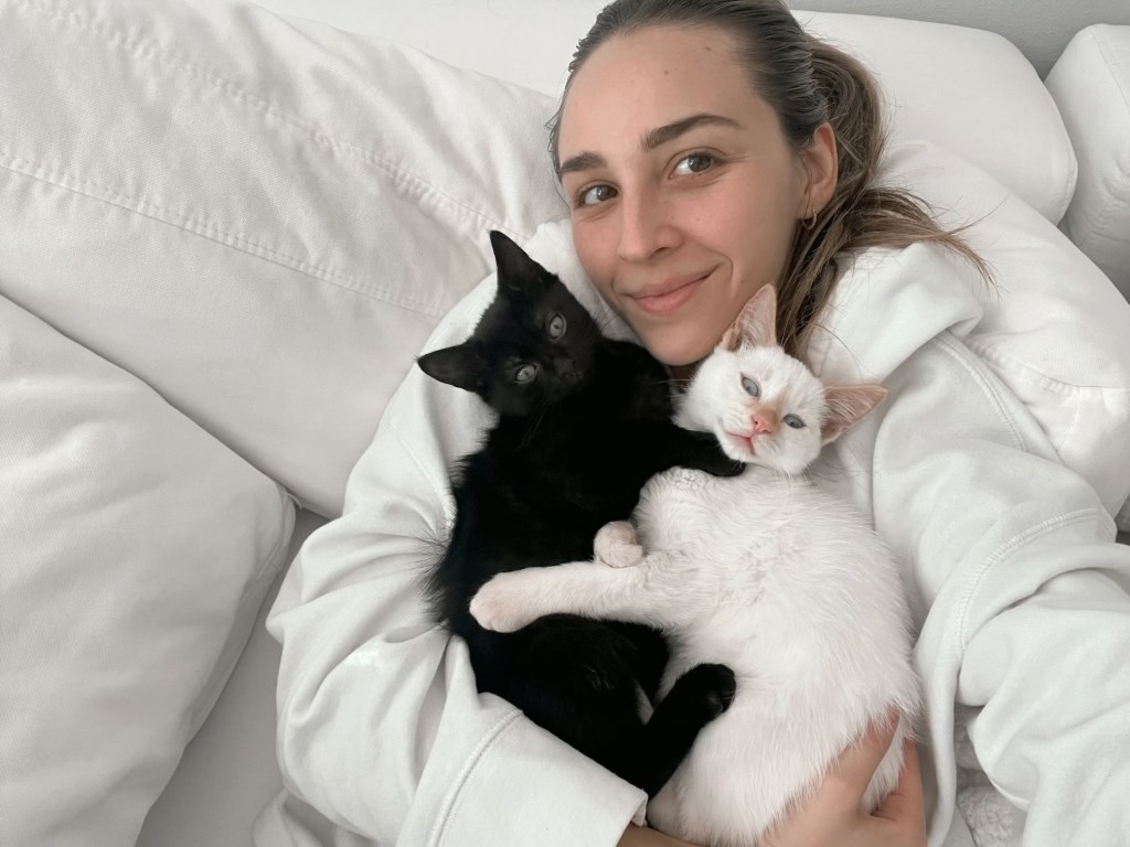 A person holding two kittens, one black and one white, while sitting on a couch with white cushions.