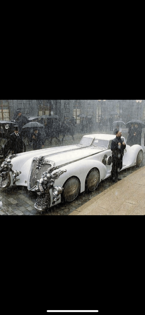 A vintage white luxury car adorned with ornate details, parked under heavy rain, with a man standing beside it, dressed formally.
