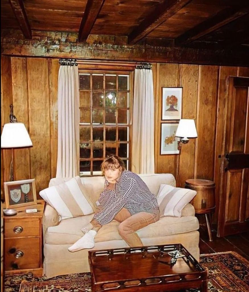 A person sitting on a sofa in a cozy wooden interior, wearing a striped shirt and relaxed pants, with a thoughtful expression.