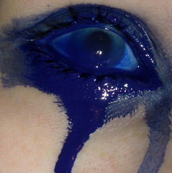 Close-up of an eye with blue paint running down the skin, creating a dramatic effect.