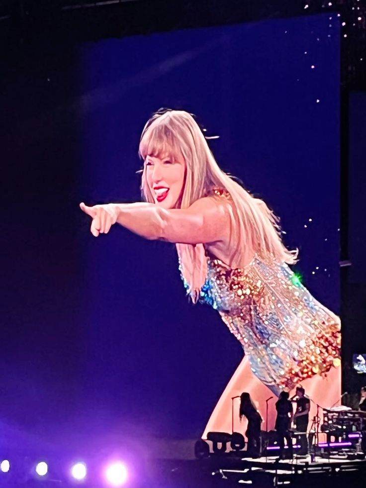 A performer pointing playfully at the audience while wearing a sparkling multicolored outfit during a concert.