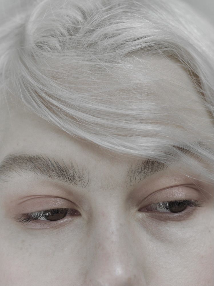Close-up of a person's face with light hair and soft makeup, showcasing their eyes and skin texture.