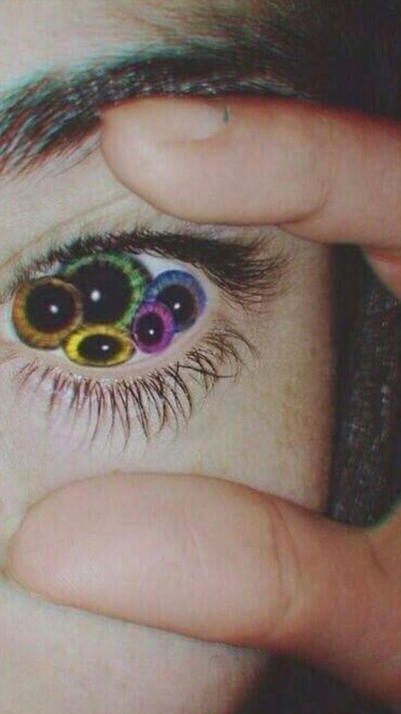 A close-up of an eye with vibrant, multi-colored lenses, partially obscured by a hand. The eye's lashes are visible, adding detail to the image.