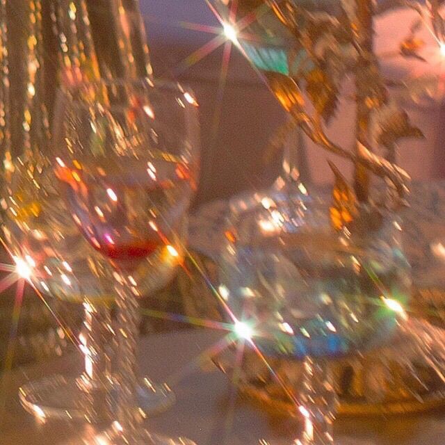 A blurred close-up of two elegant glassware items, one containing a red drink, with sparkling light reflections in a soft-focus background.